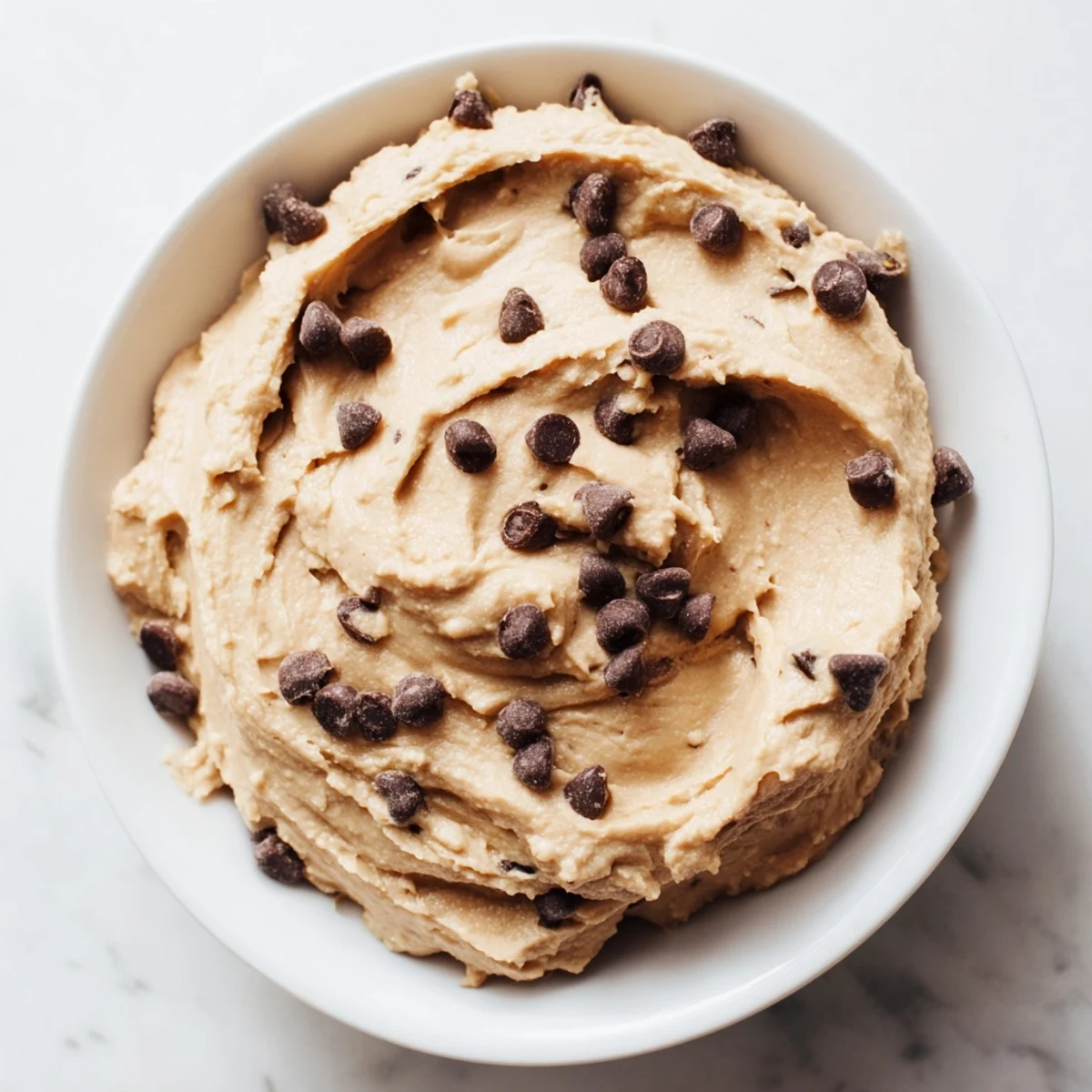 Smooth and creamy Chocolate Chip Cookie Dough Hummus with mini chocolate chips in a white serving bowl.