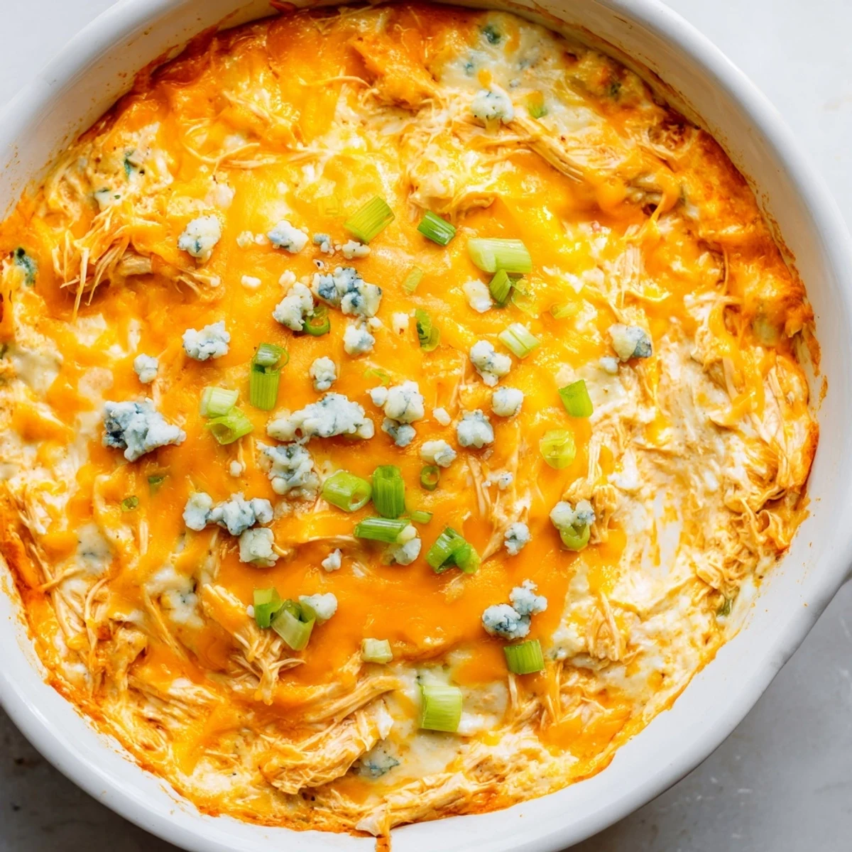 Golden, bubbly Spicy Buffalo Chicken Dip in a white baking dish, served with a pile of crispy tortilla chips for dipping. 