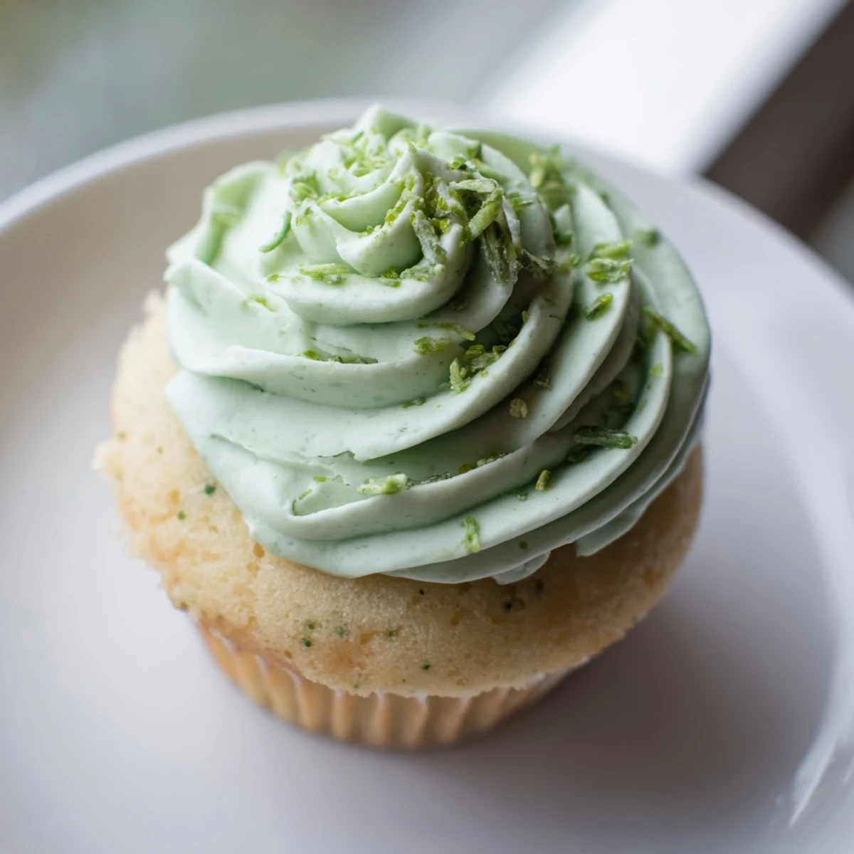 A Shamrock Shake Cupcake with a bite taken out, revealing a fluffy vanilla crumb.