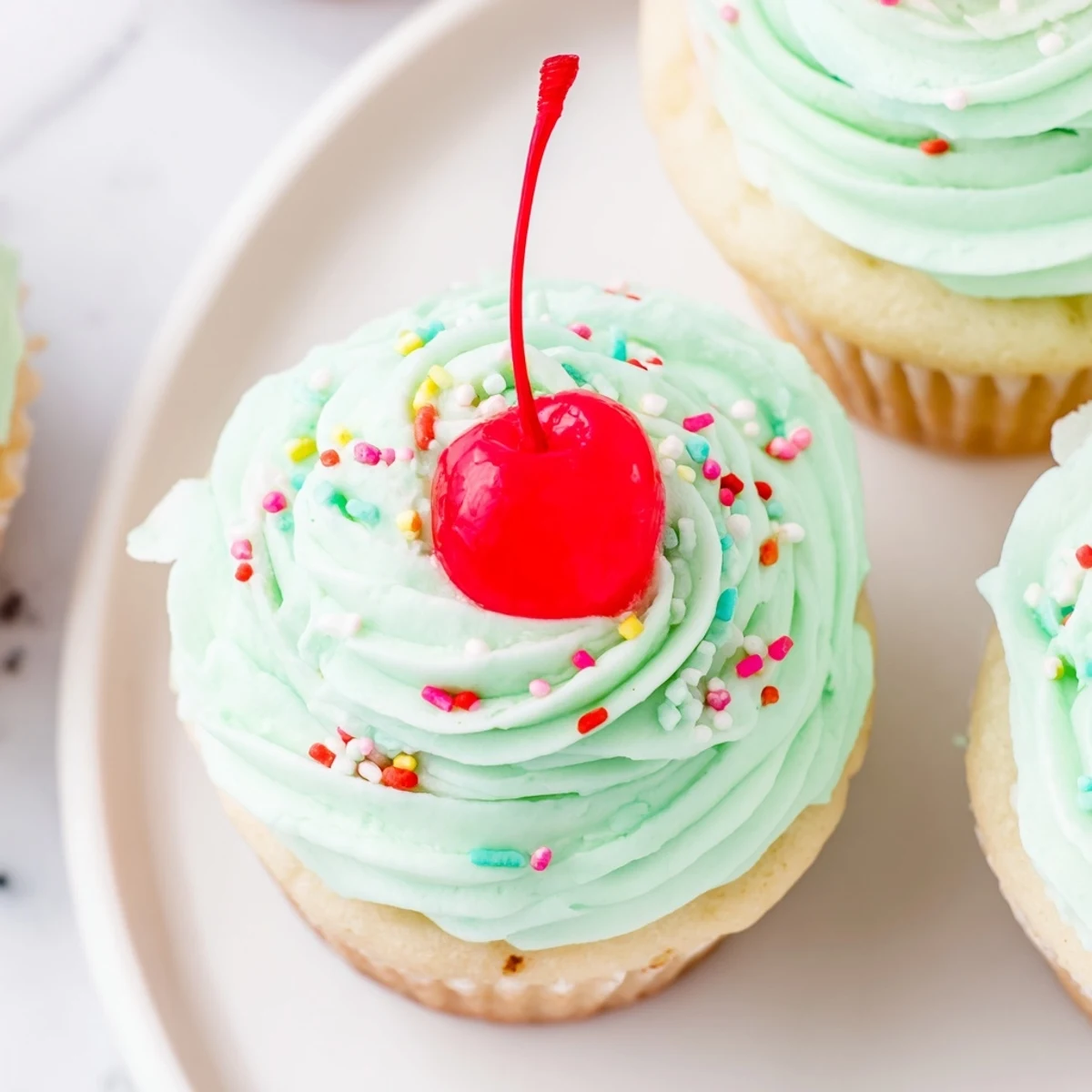 Moist Shamrock Shake Cupcakes with mint frosting are topped with bright green sprinkles and a mini straw, perfect for St. Patrick's Day parties.