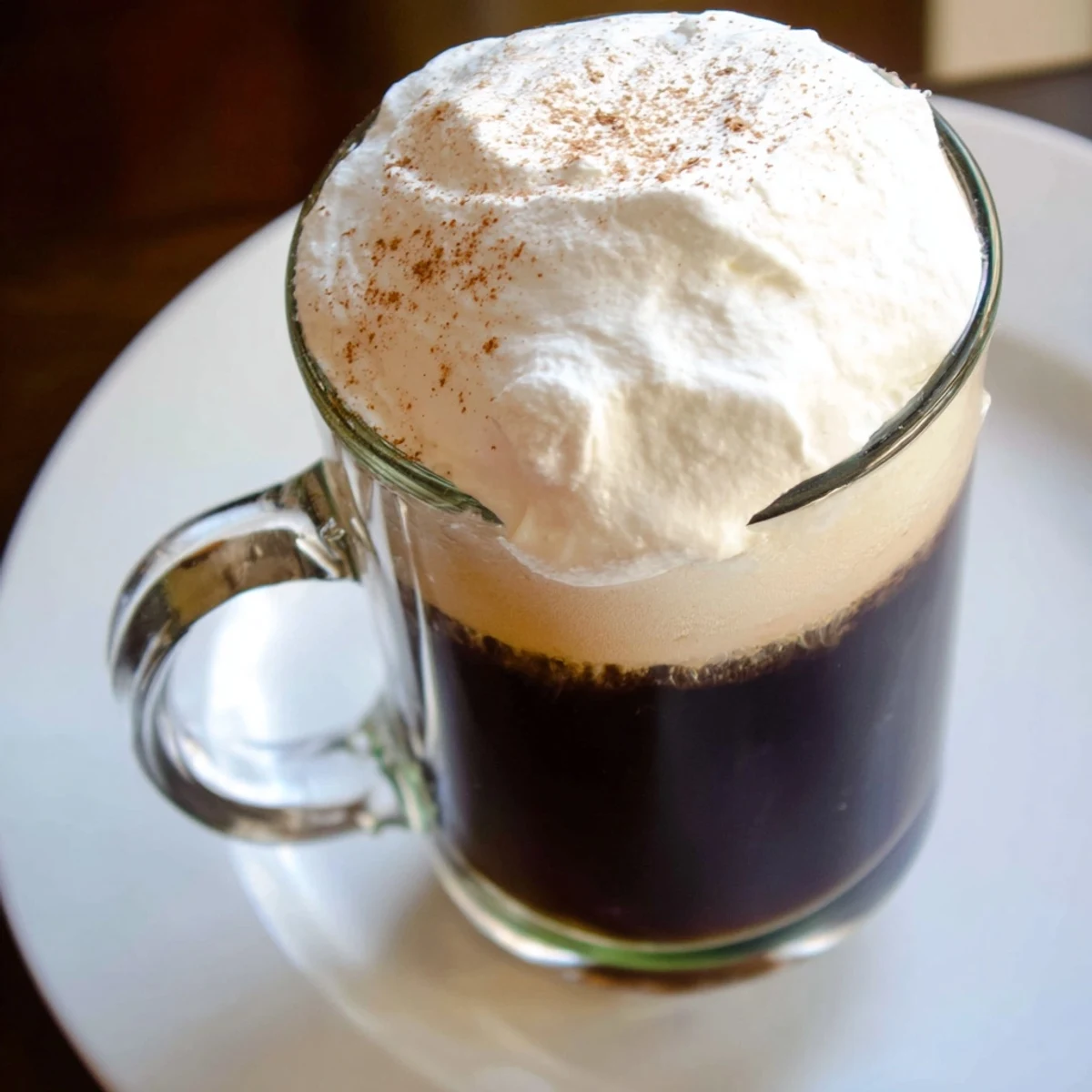 A close-up of an Irish Coffee Mocktail with Whipped Cream, steaming coffee and fluffy white topping in a glass.
