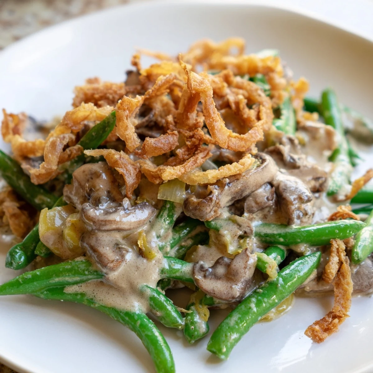A close-up of the classic Green Bean Casserole with Crispy Onions, showcasing the creamy mushroom sauce coating tender green beans under a golden-brown topping.