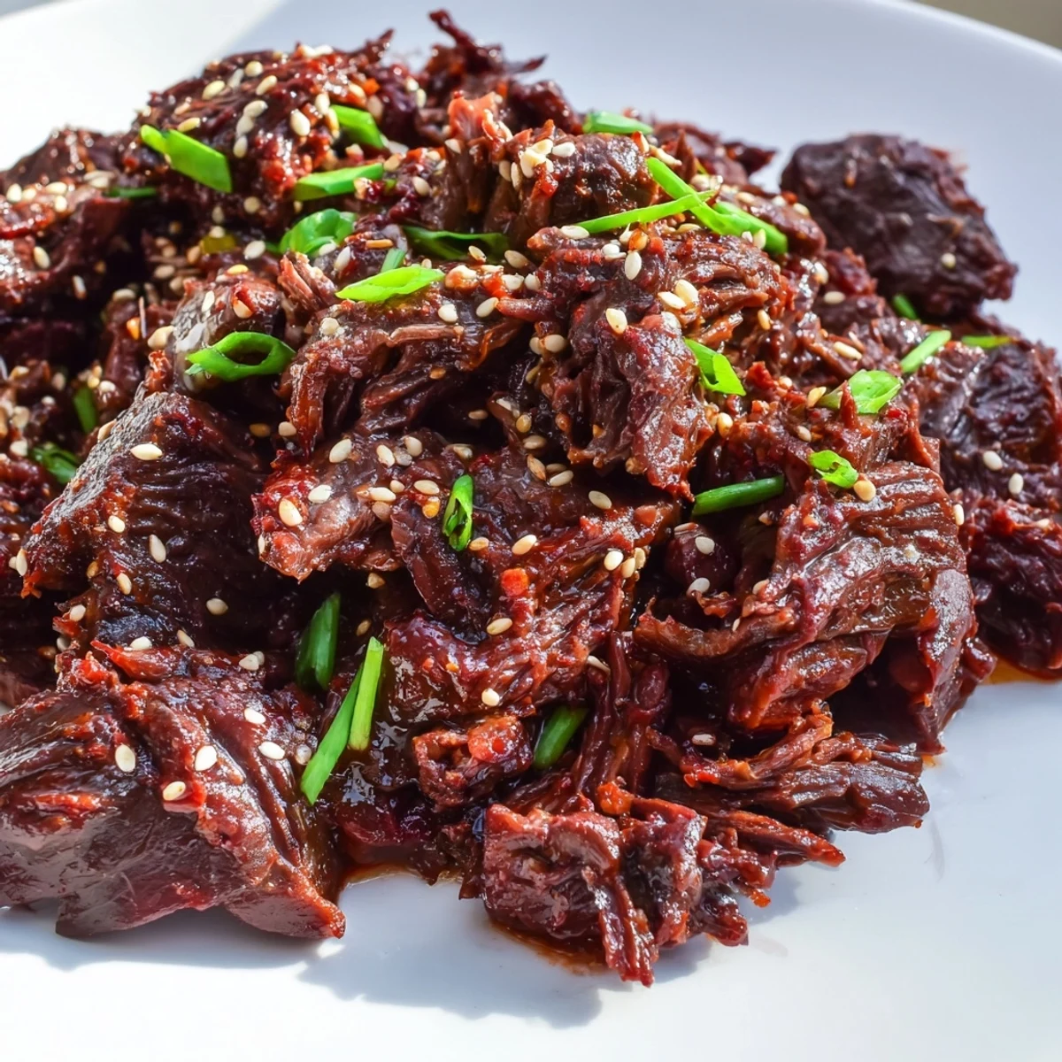 Golden-brown shredded Crock Pot Korean Beef piled high on a bed of fluffy white rice, garnished with green onions and sesame seeds.
