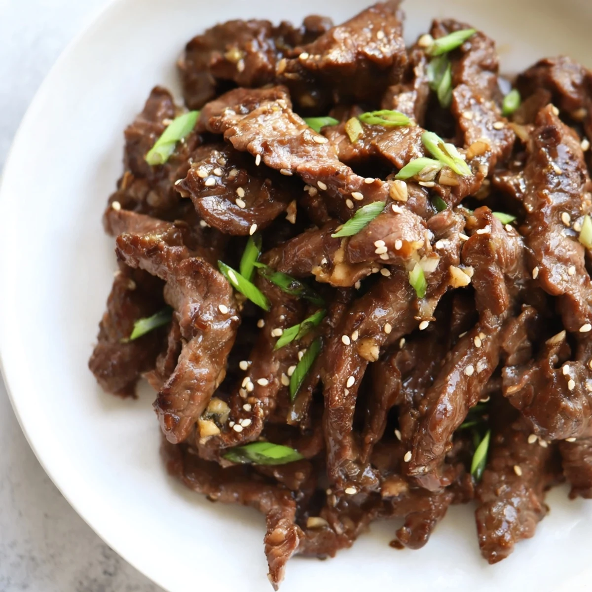 Tender beef slices coated in a glossy, sweet-savory Mongolian Beef sauce, garnished with green onions and sesame seeds, served over fluffy white rice.