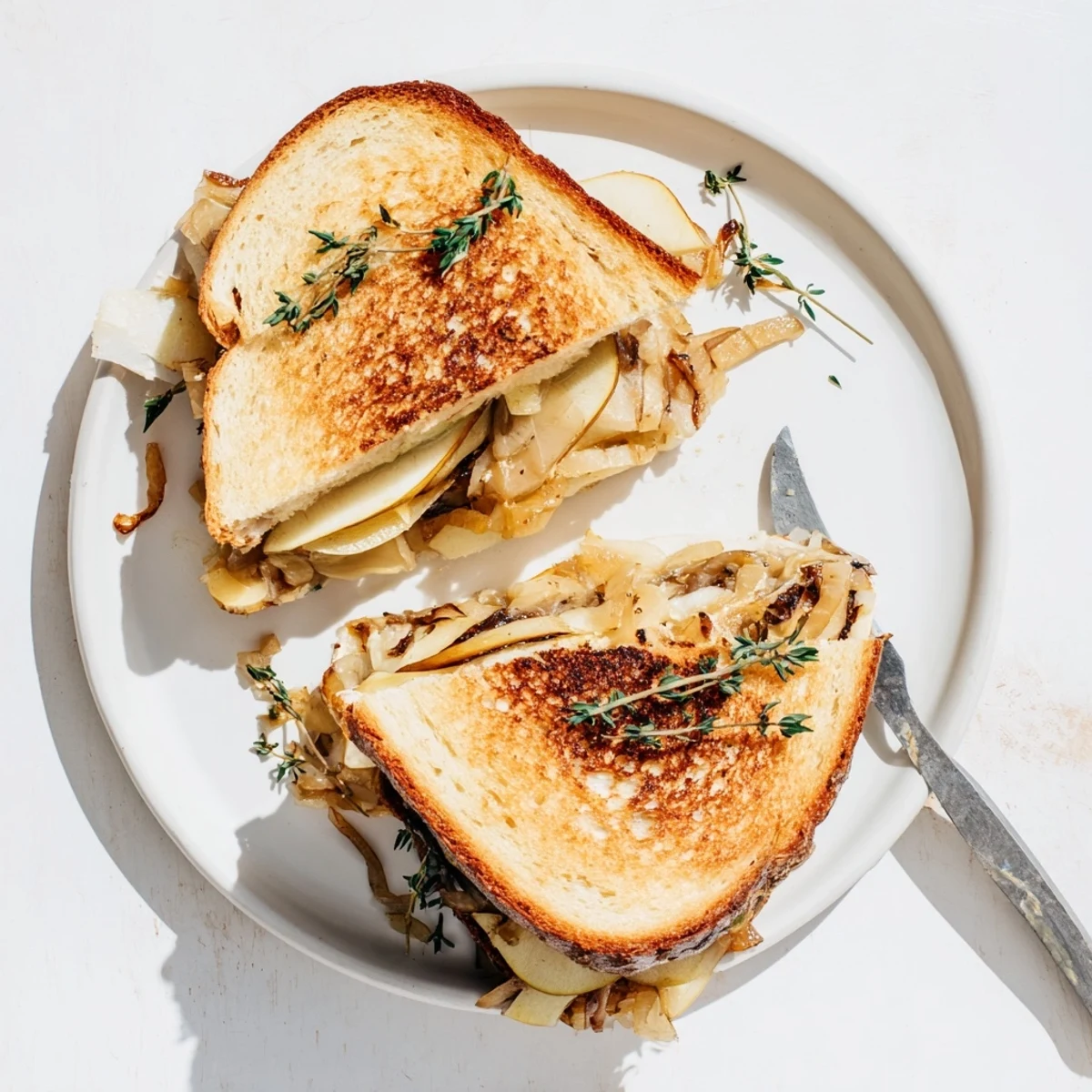 Golden-brown grilled bread holding melted cheddar, sweet pear, apple slices, and savory caramelized onions for a gourmet sandwich.