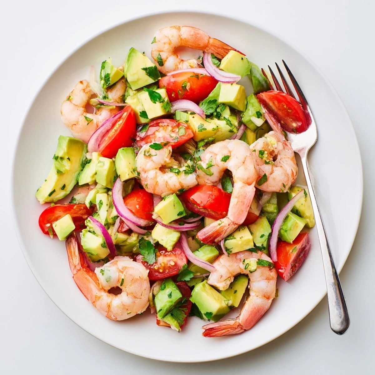 Fresh Healthy Shrimp Avocado Salad featuring succulent shrimp, cherry tomatoes, cucumber, and creamy avocado chunks on a white plate.