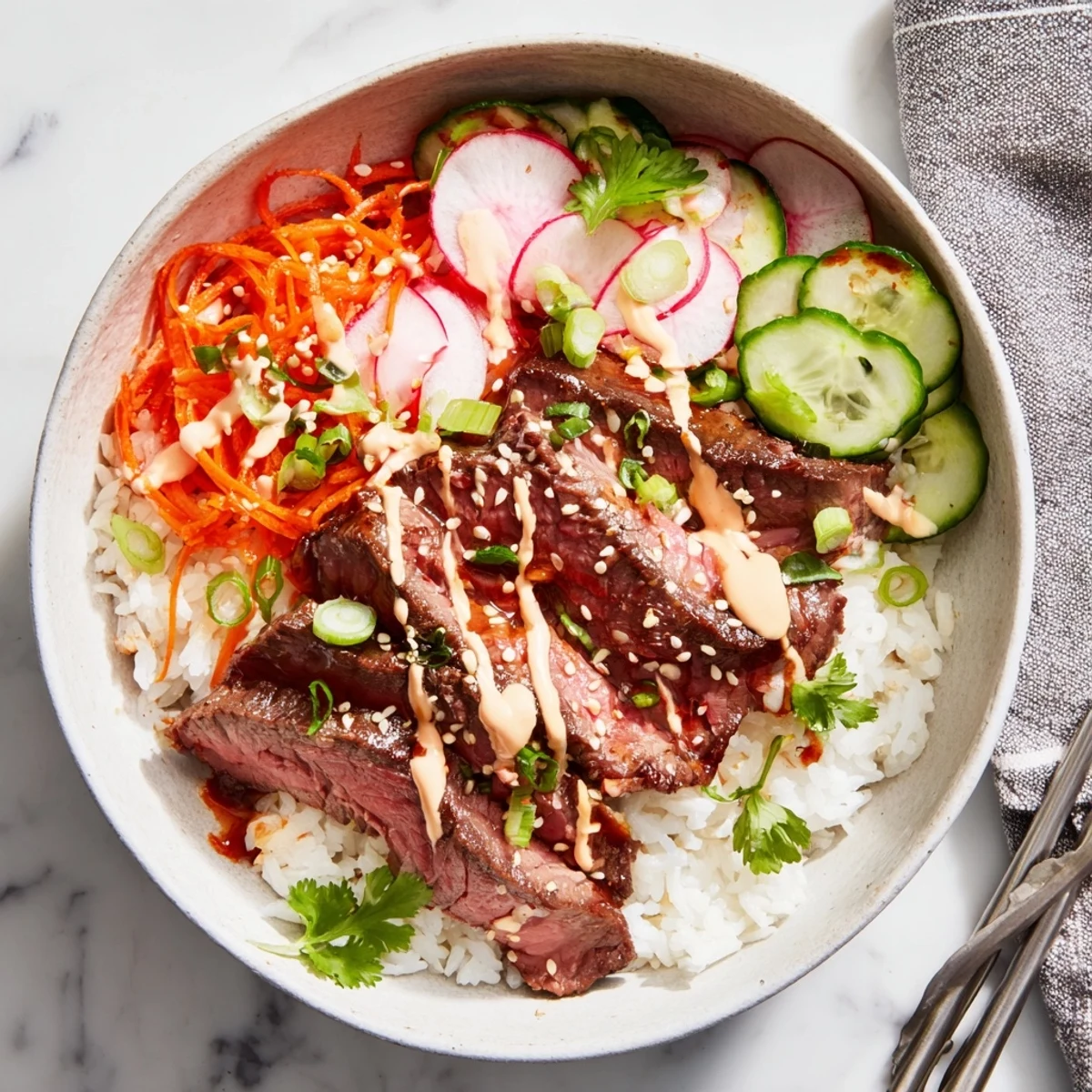 Freshly seared, tender marinated steak rests atop fluffy rice with crunchy carrots and cucumbers, ready for the spicy cream sauce drizzle in this Korean BBQ Steak Rice Bowls bowl.