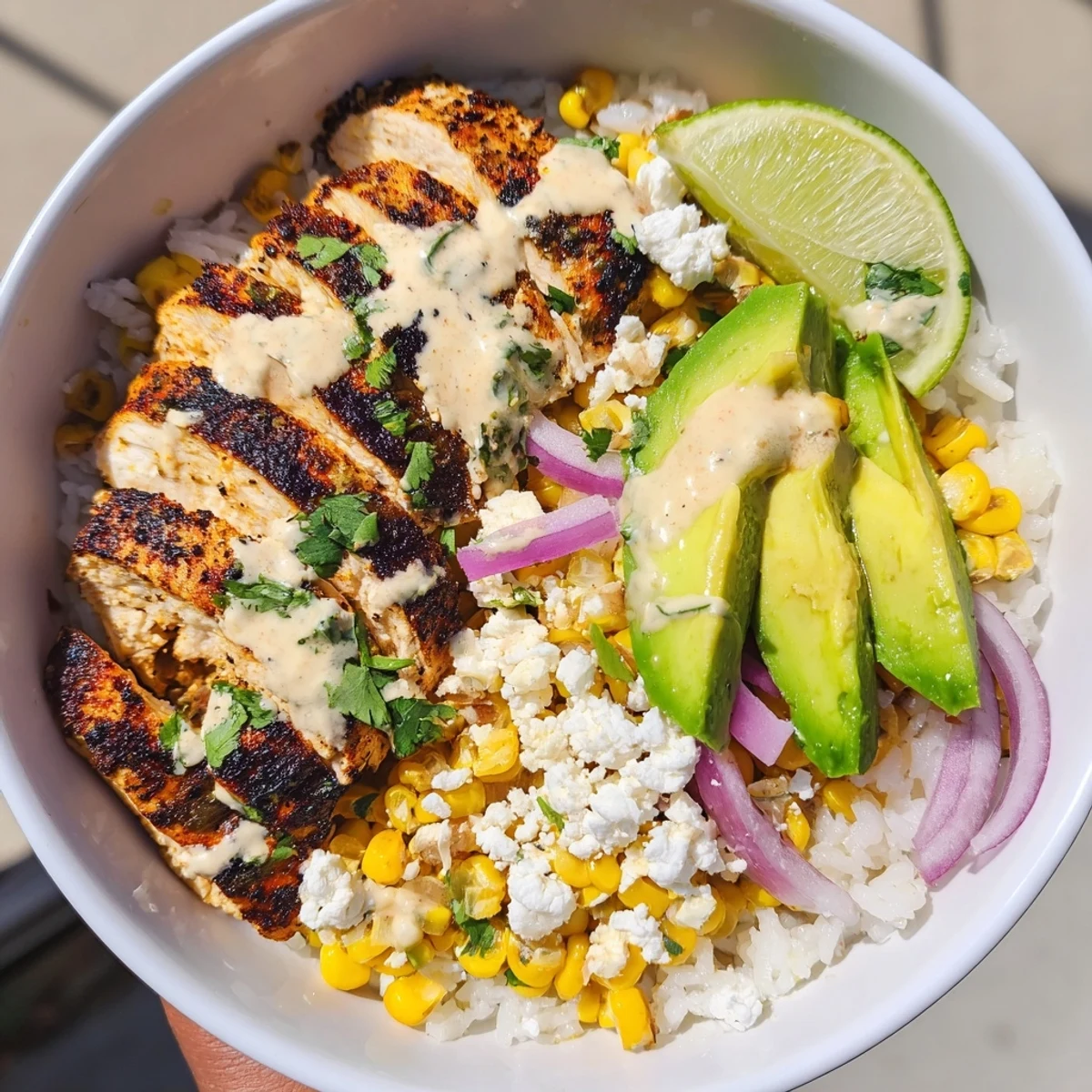 Savory street corn chicken rice bowl arranged with charred corn, sliced chicken, and lime wedges