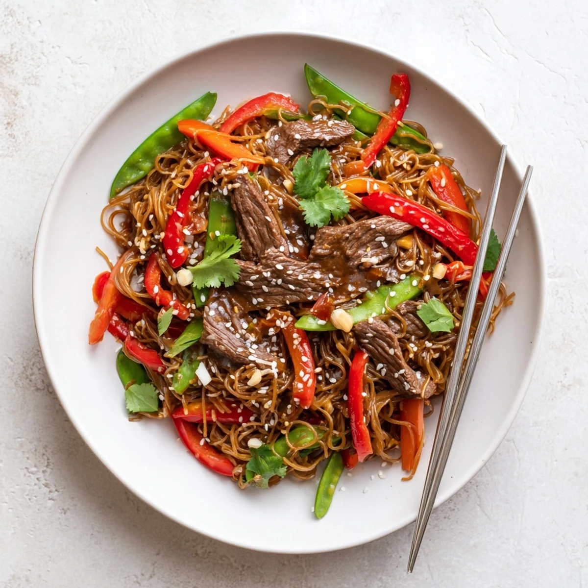 Plate of sticky beef noodles garnished with sesame seeds and fresh cilantro leaves