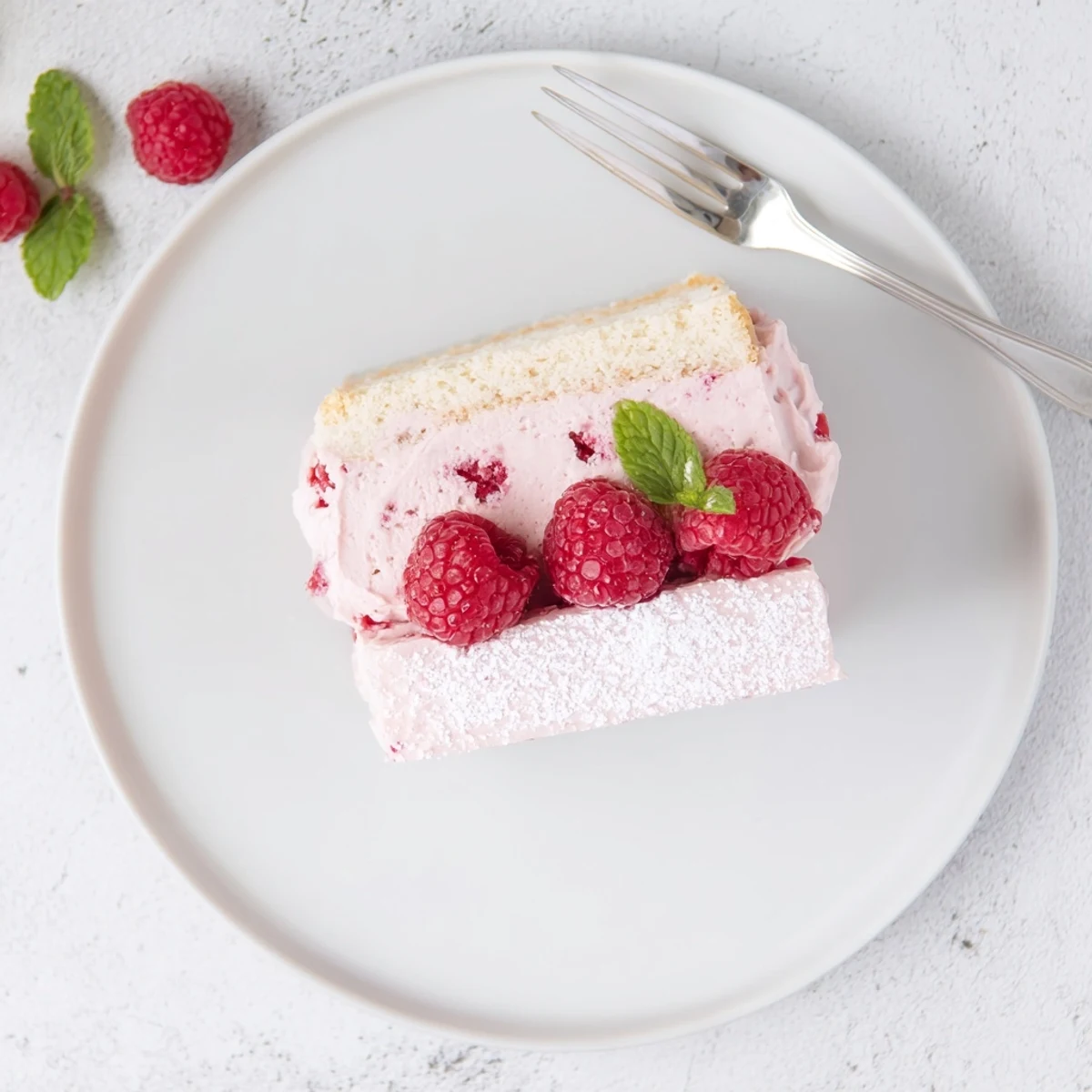 Homemade raspberry mousse cake garnished with fresh raspberries and mint on white serving plate