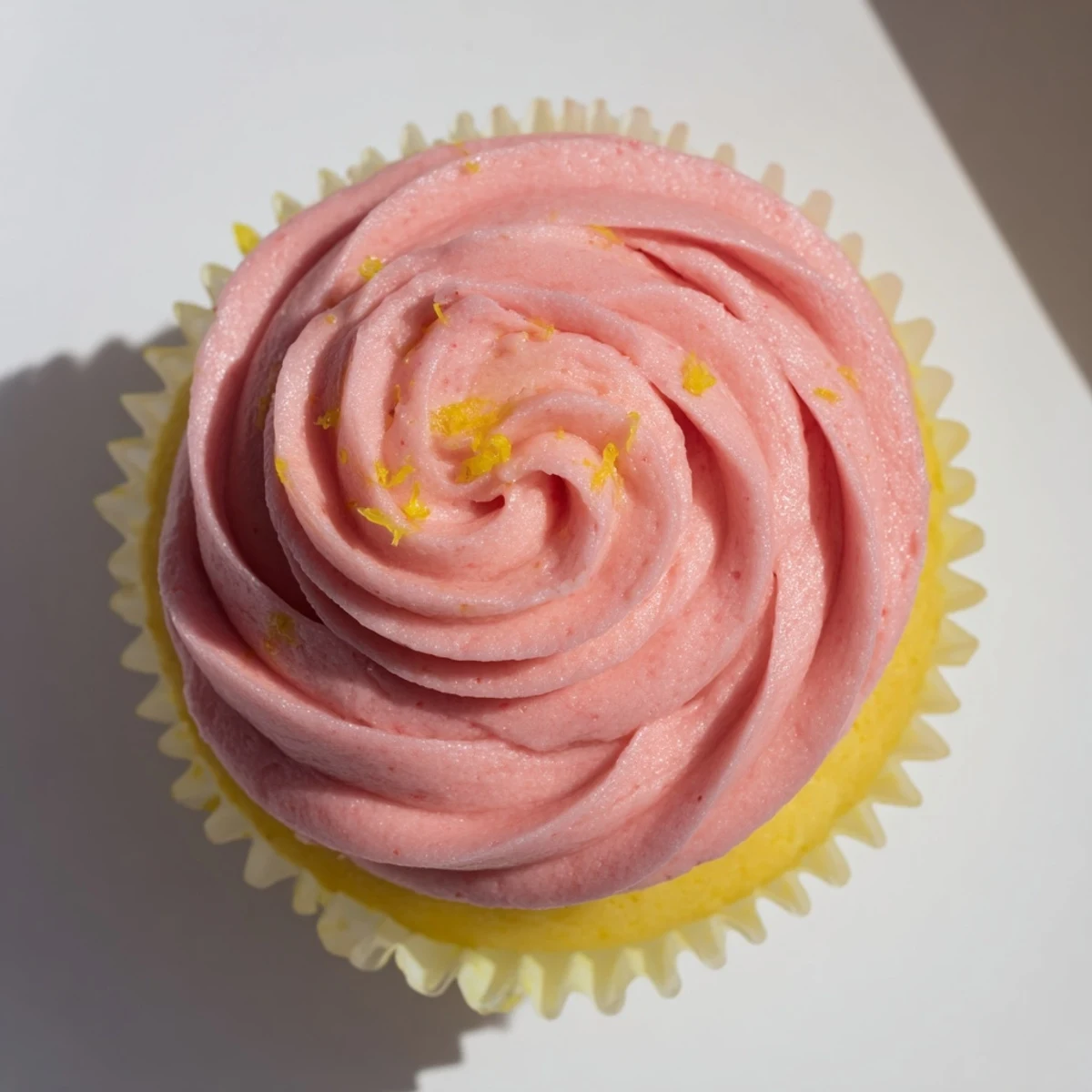 Golden lemon cupcakes with swirls of fresh strawberry buttercream frosting on a white plate