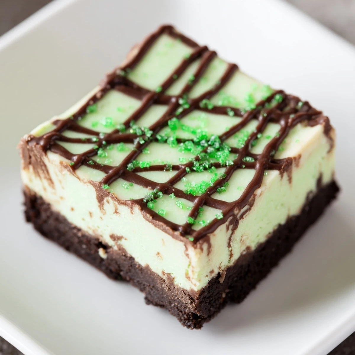 Rich green mint cheesecake fudge squares on dark chocolate cookie crust with festive drizzle