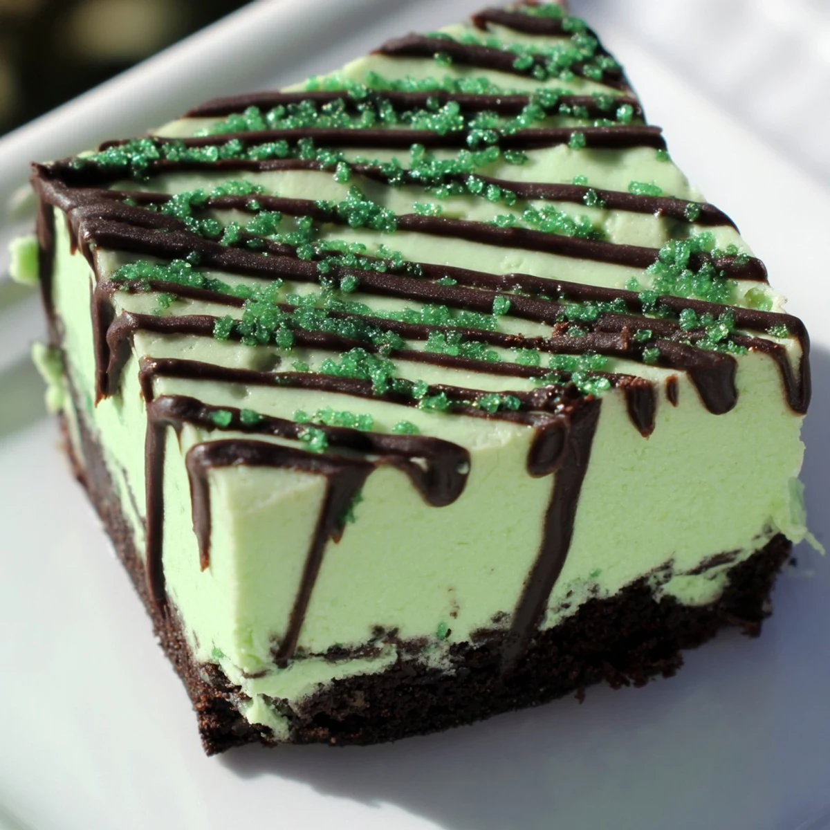 Creamy Irish cheesecake fudge bars topped with dark chocolate and green sprinkles on white plate