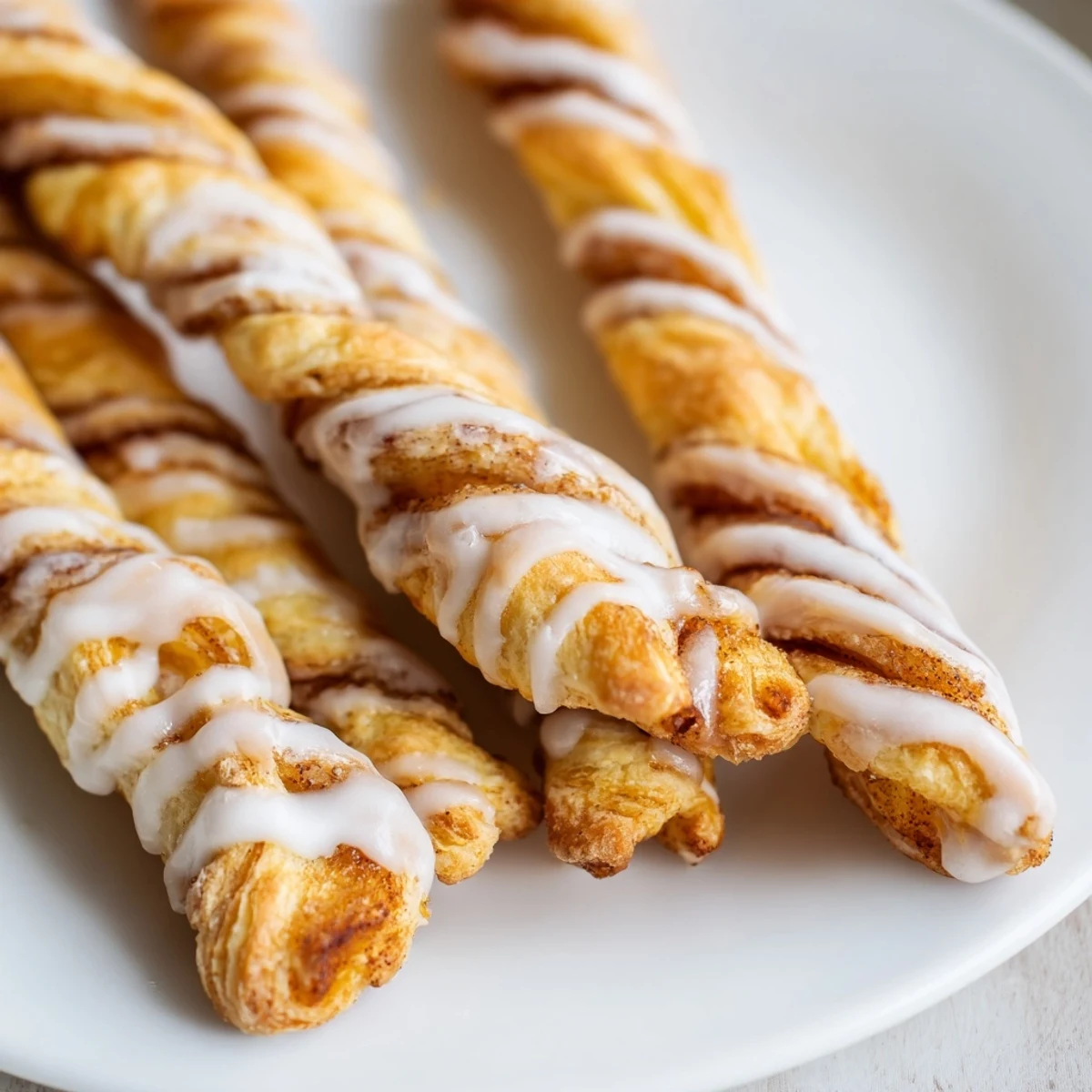 Warm homemade cinnamon sugar twists arranged on a baking sheet with vanilla glaze dripping