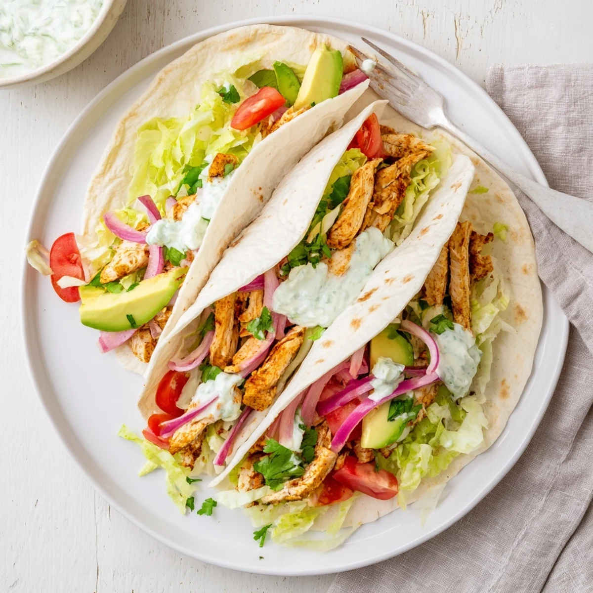 Spicy chicken avocado wraps served halved on a white plate with spicy sauce drizzle