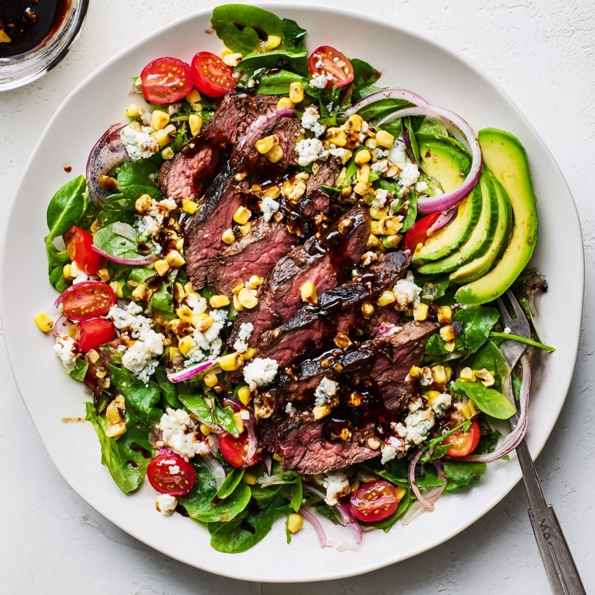 Sliced balsamic-marinated flank steak atop crisp greens with crumbled Gorgonzola in a balsamic steak Gorgonzola salad with grilled corn.