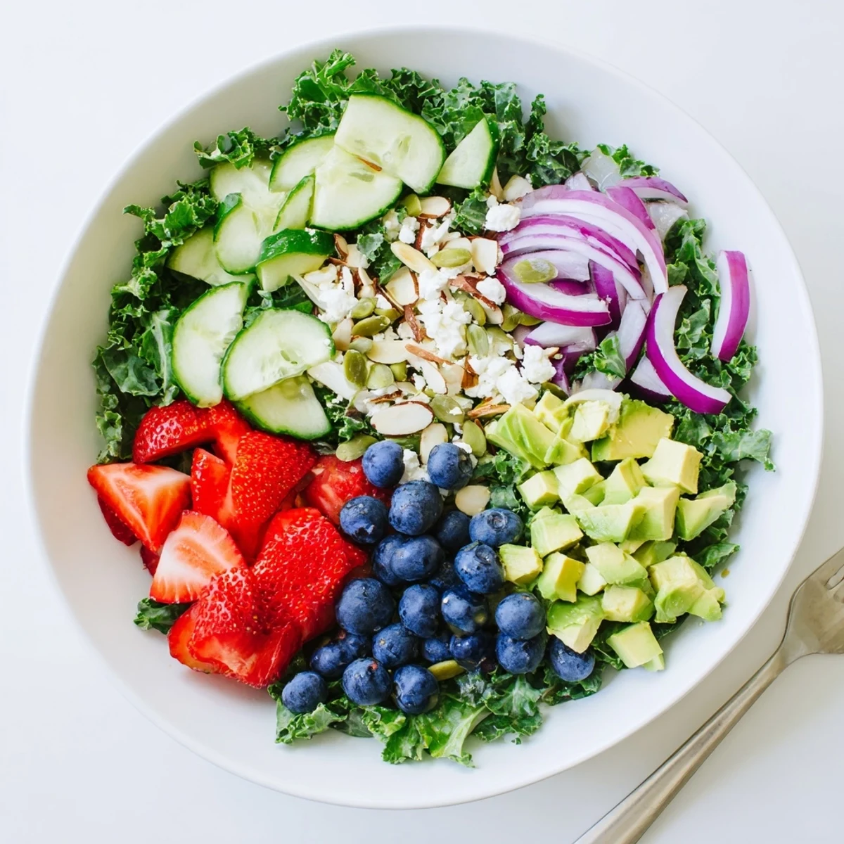 A colorful summer kale salad topped with feta, berries, and toasted almonds