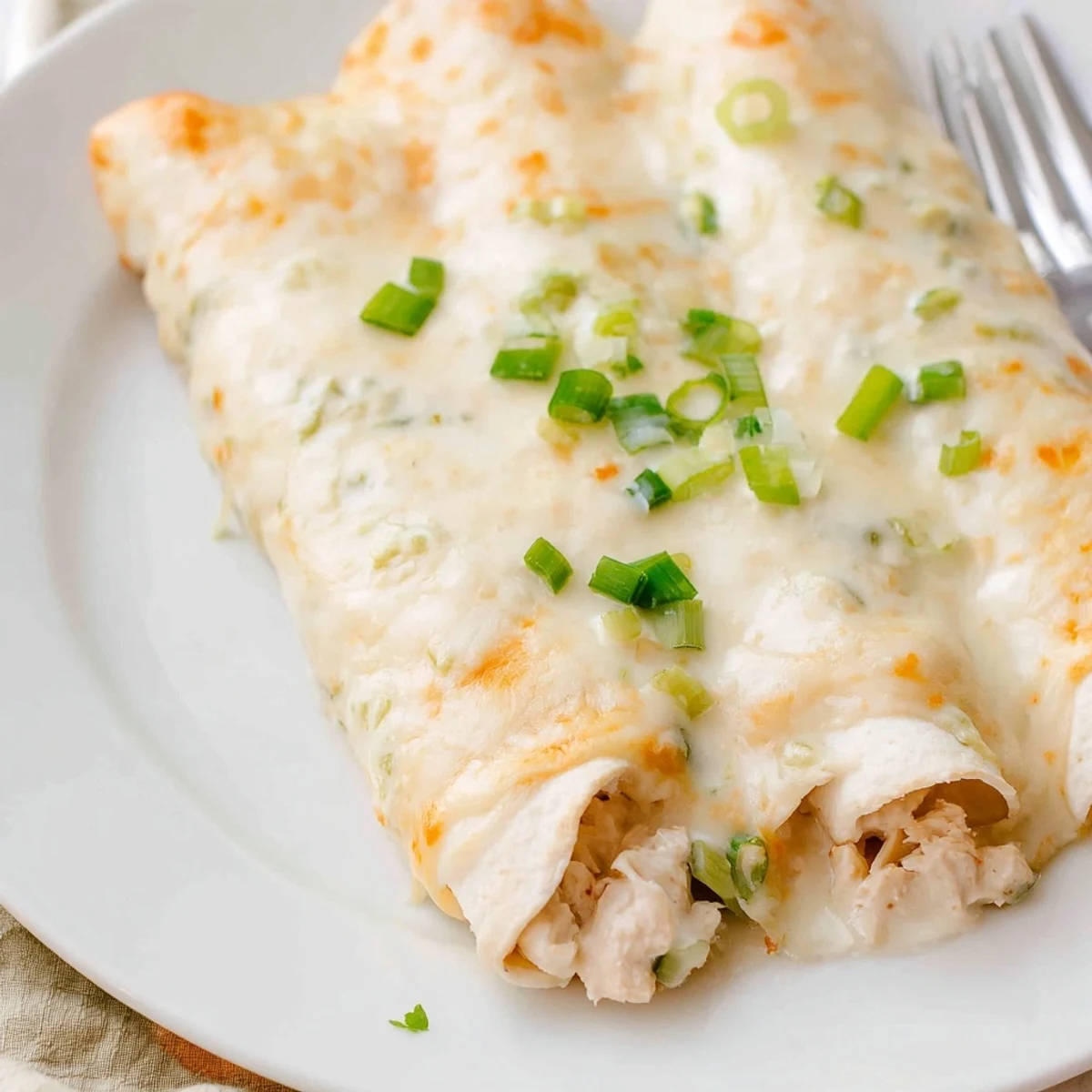 Baked Creamy White Chicken Enchiladas on a plate, creamy sauce visible