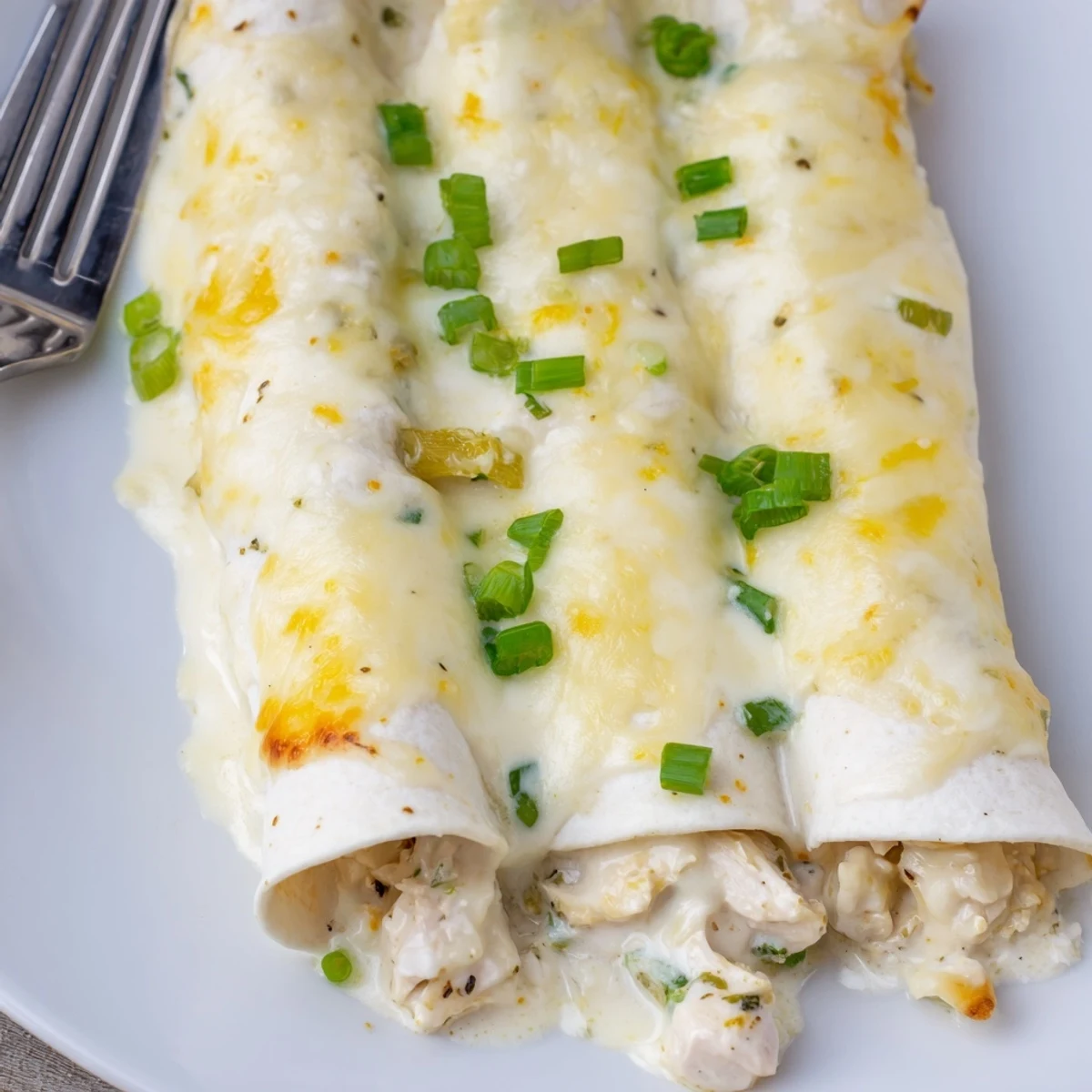 Creamy White Chicken Enchiladas bubbling golden, topped with cilantro and sliced green onions