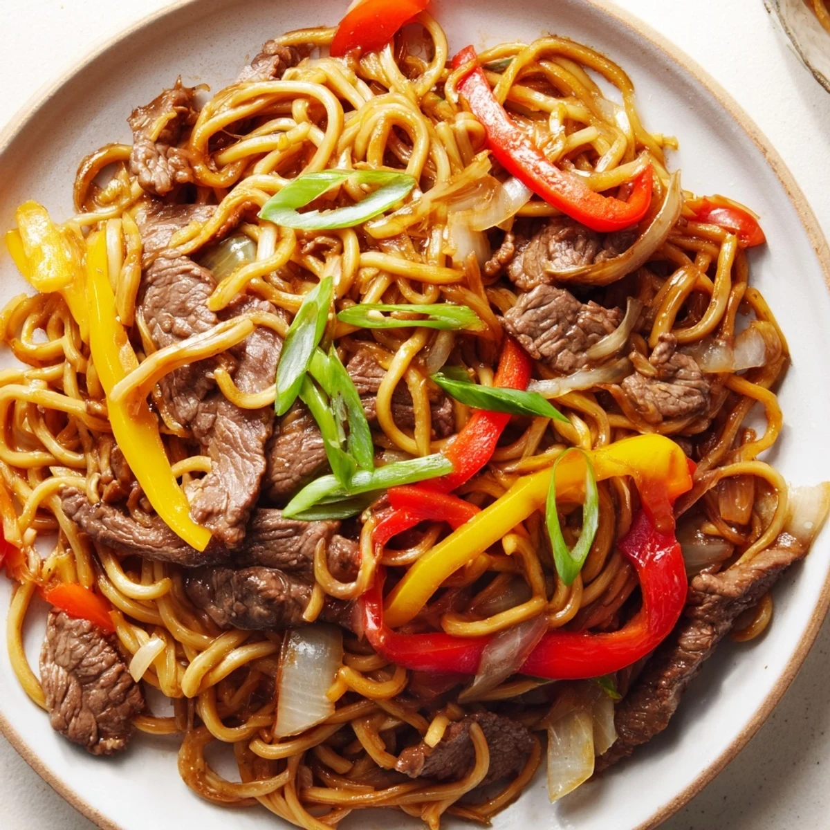 Plate of beef chow mein with peppers and onions tossed in glossy savory sauce
