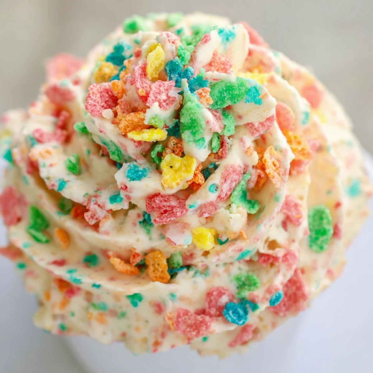Colorful Fruity Pebbles cereal frosting piped onto cupcakes with crunchy rainbow cereal garnish