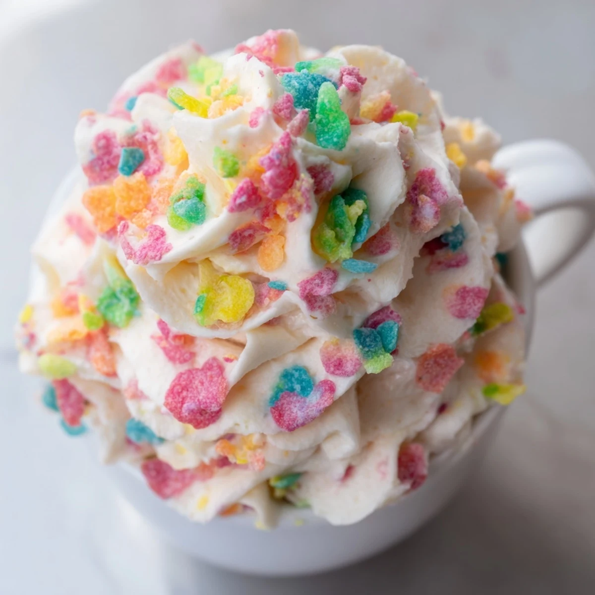 Swirled buttercream frosting studded with rainbow Fruity Pebbles cereal garnishing a freshly baked cupcake