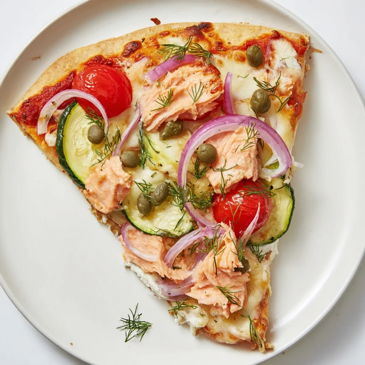 Sliced leftover salmon tortilla pizza garnished with fresh dill and zucchini on a board.