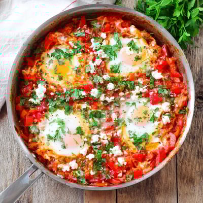 A rustic wooden table displays Quick Shakshuka Eggs, garnished with fresh parsley and served alongside warm, crusty bread for dipping.