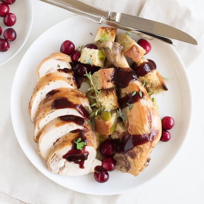 Juicy Cherry Roast Chicken carved and served with savory sage stuffing and vibrant cherry sauce alongside roasted root vegetables. 