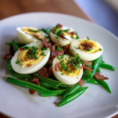 The Green Bean, Bacon, and Egg Salad is plated on a white dish, drizzled with a tangy Dijon vinaigrette and garnished with fresh parsley.